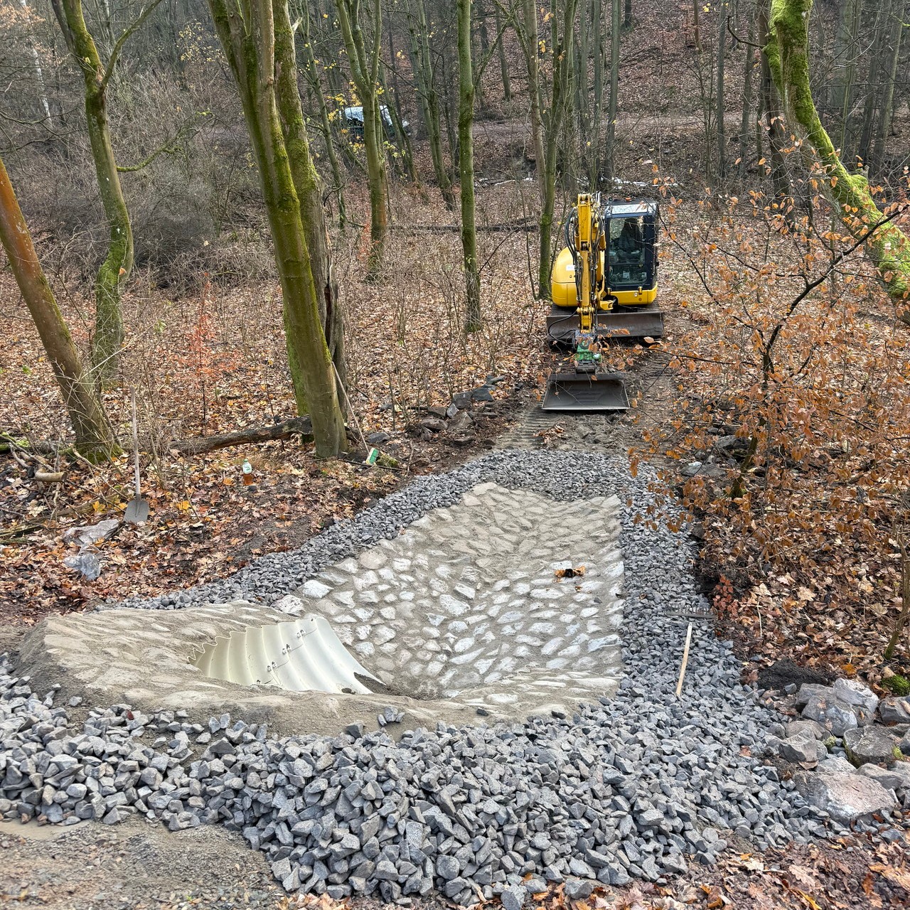Wasserbauarbeiten mit Natursteinrinne und Bagger im Gelände